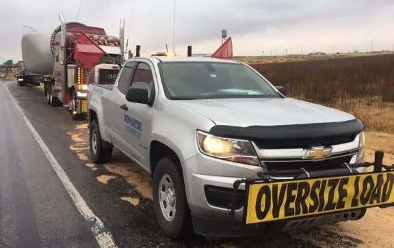 Bonafide pilot truck with an oversize load sign beside a semi on the highway