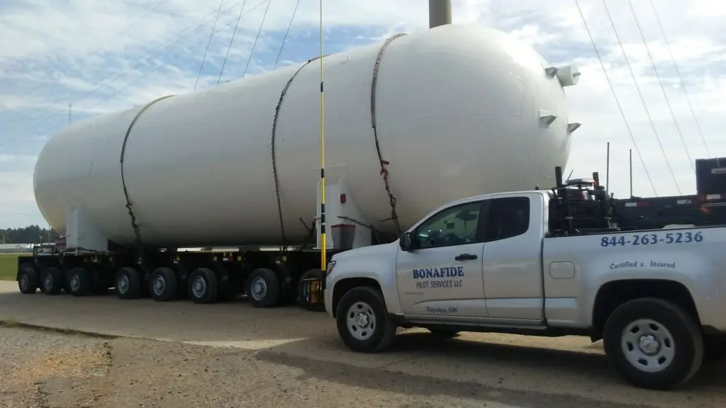 Bonafide escort beside a large white pressure vessel on a multi-axle trailer