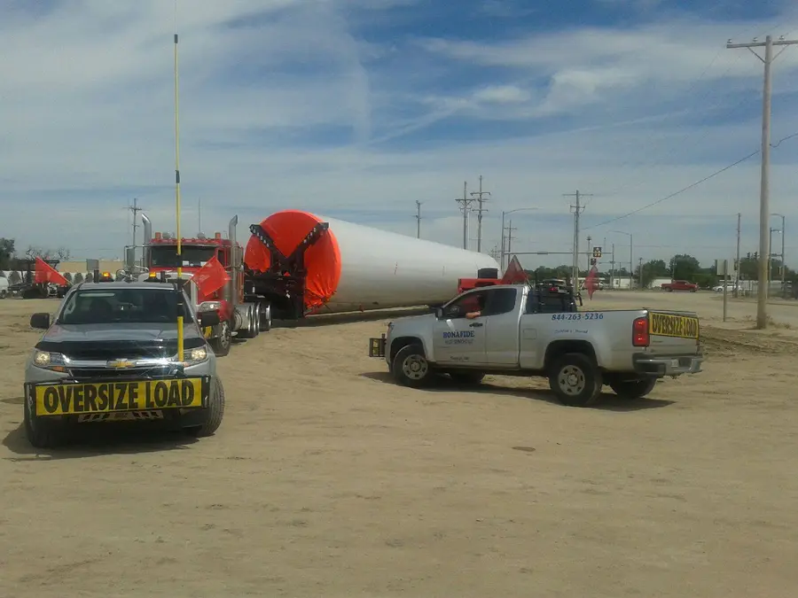 Bonafide pilot truck with an oversize sign beside a wind tower section